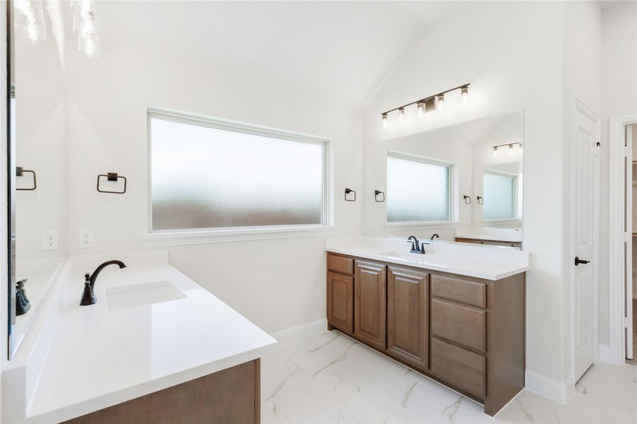 Bathroom with dual vanities, wood cabinets, white countertops, vaulted ceiling, and marble tile floors Bathroom with dual vanities, wood cabinets, white countertops, vaulted ceiling, and marble tile floors