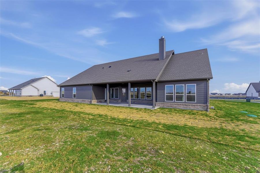 Back of house featuring a lawn, a patio area, a chimney, and brick siding