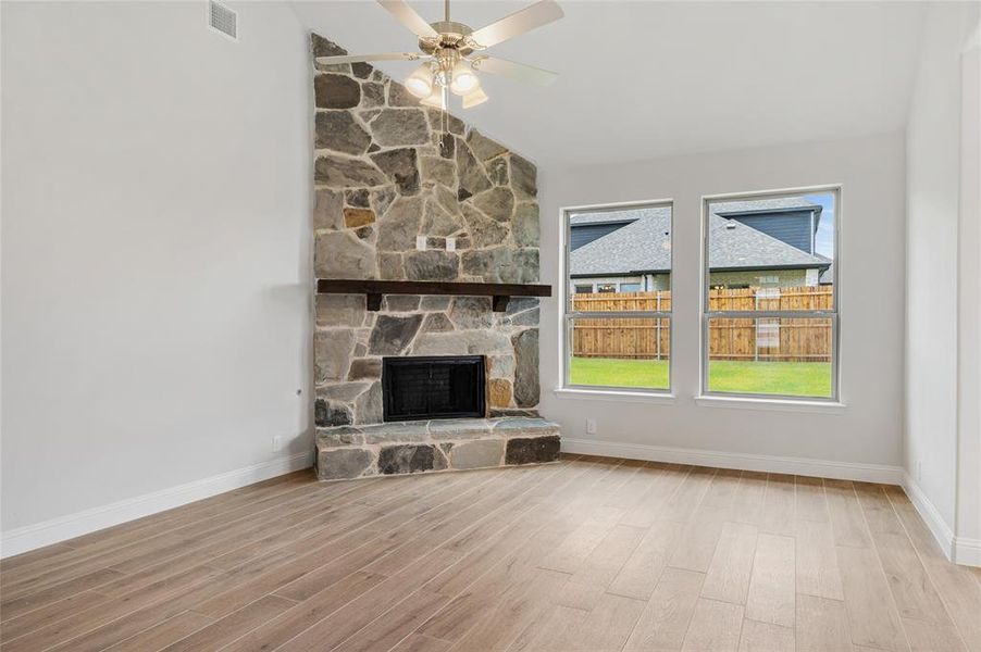 Unfurnished living room with a fireplace, vaulted ceiling, light wood-style flooring, and ceiling fan