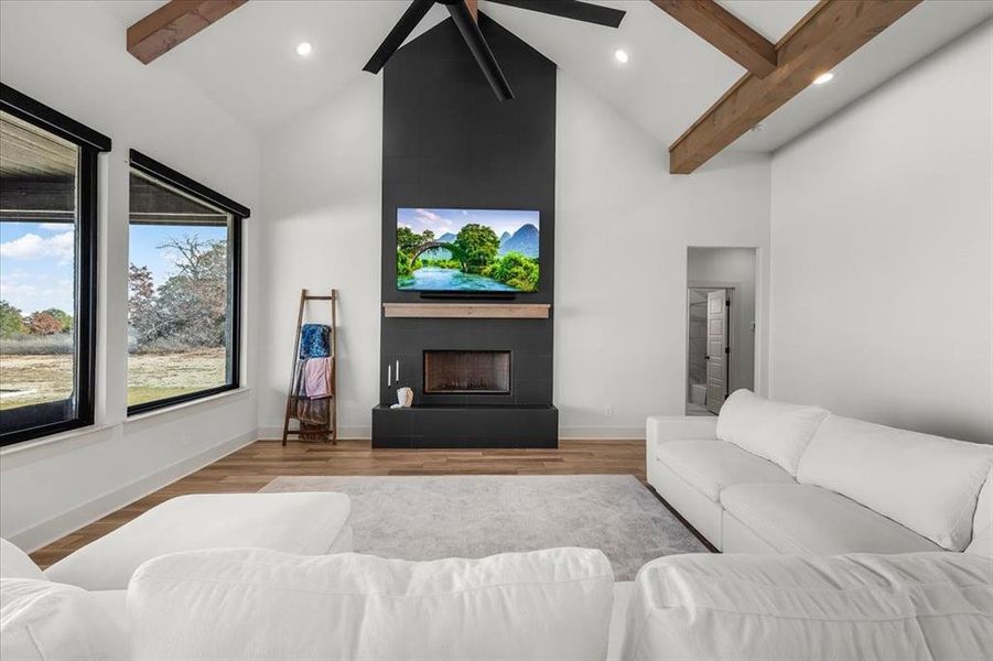 Living room featuring vaulted ceiling with beams, ceiling fan, light hardwood / wood-style floors, and a tiled fireplace