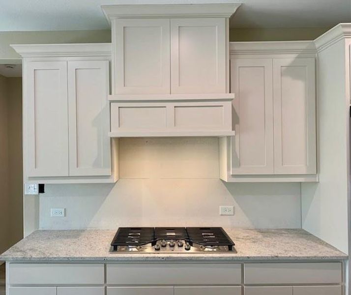 Kitchen with light stone counters, white cabinetry, and stainless steel gas cooktop