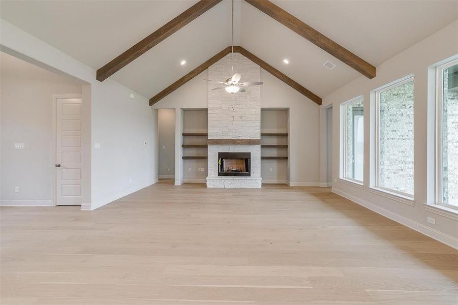 Unfurnished living room with a fireplace, light wood-type flooring, built in shelves, beam ceiling, and ceiling fan