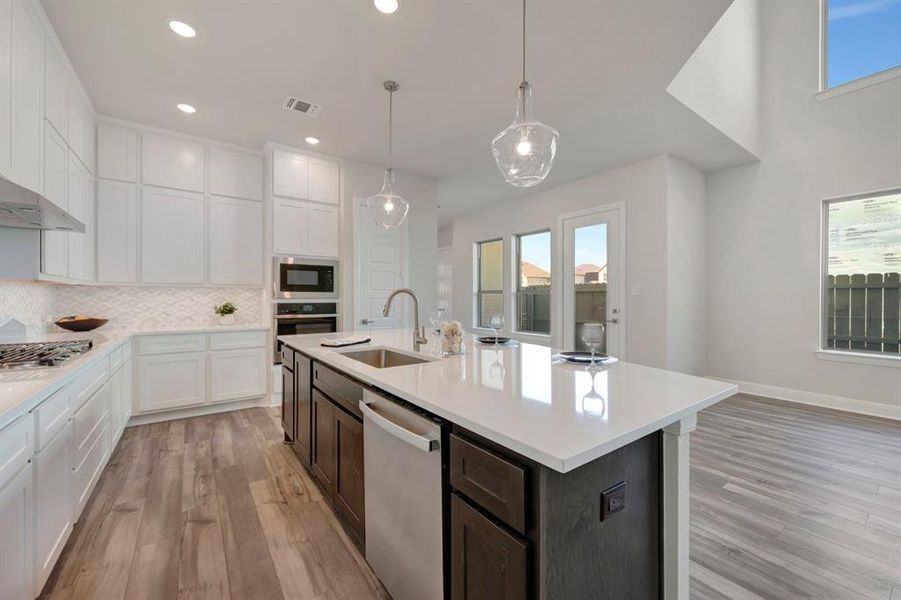 Kitchen featuring two tone cabinetry, backsplash, stainless steel appliances, light wood-type flooring, and decorative light fixtures
