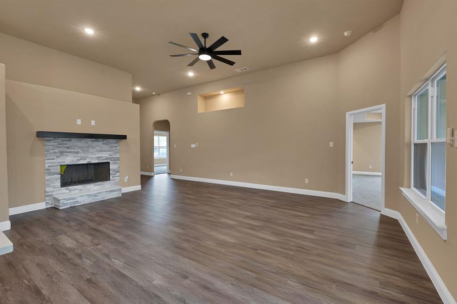 Unfurnished living room featuring a stone fireplace, a ceiling fan, arched walkways, dark wood-type flooring, and baseboards Unfurnished living room featuring a stone fireplace, a ceiling fan, arched walkways, dark wood-type flooring, and baseboards