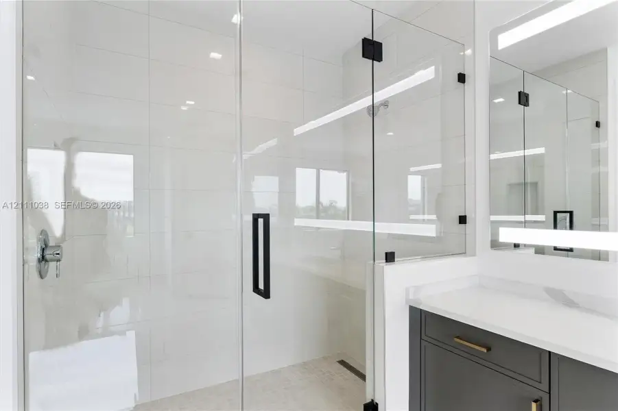 Walk-in shower with floor-to-ceiling tile, frameless glass enclosure, and matte black hardware, featuring a modern vanity with a white countertop and integrated linear LED mirror lighting