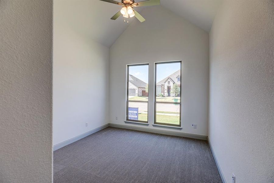 Empty room with a textured wall, a ceiling fan, carpet flooring, and lofted ceiling Empty room with a textured wall, a ceiling fan, carpet flooring, and lofted ceiling