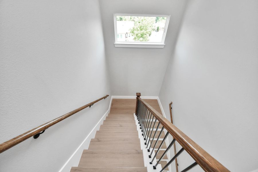Modern staircase featuring warm wood accents, sleek metal railings, & abundant natural light for a clean contemporary feel throughout the home.