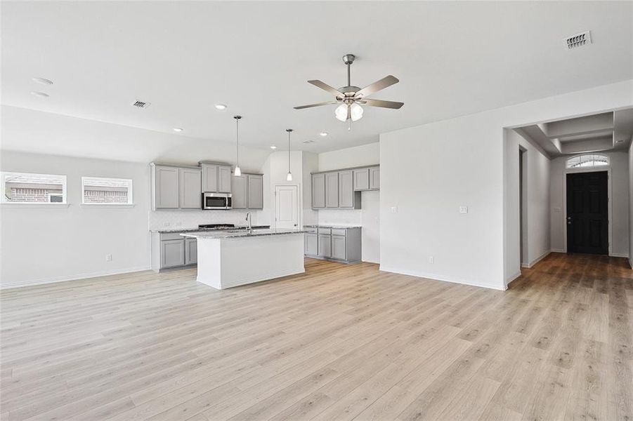 Kitchen featuring pendant lighting, ceiling fan, a center island with sink, gray cabinetry, and light hardwood / wood-style floors