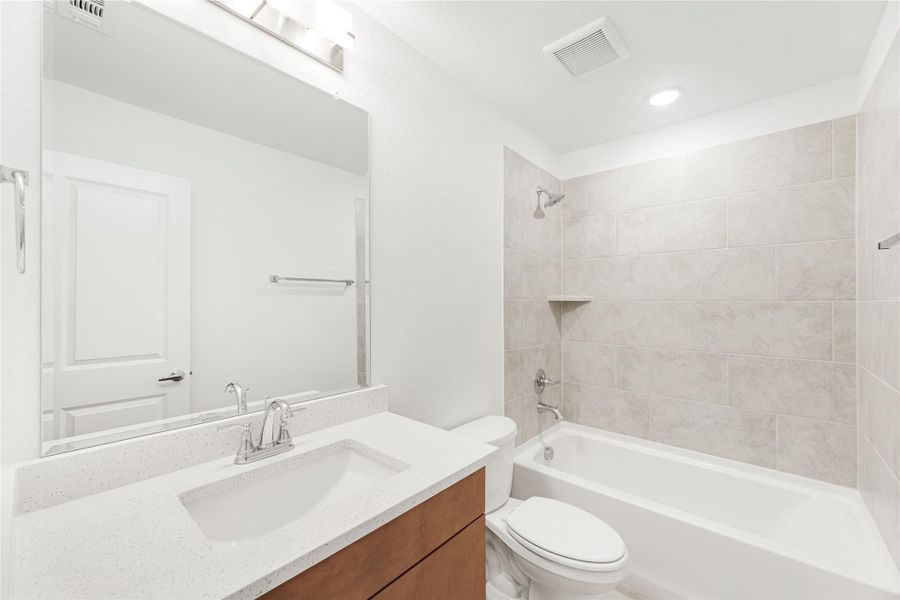 Bathroom with single vanity, quartz countertop, and tiled shower-tub combo with chrome fixtures