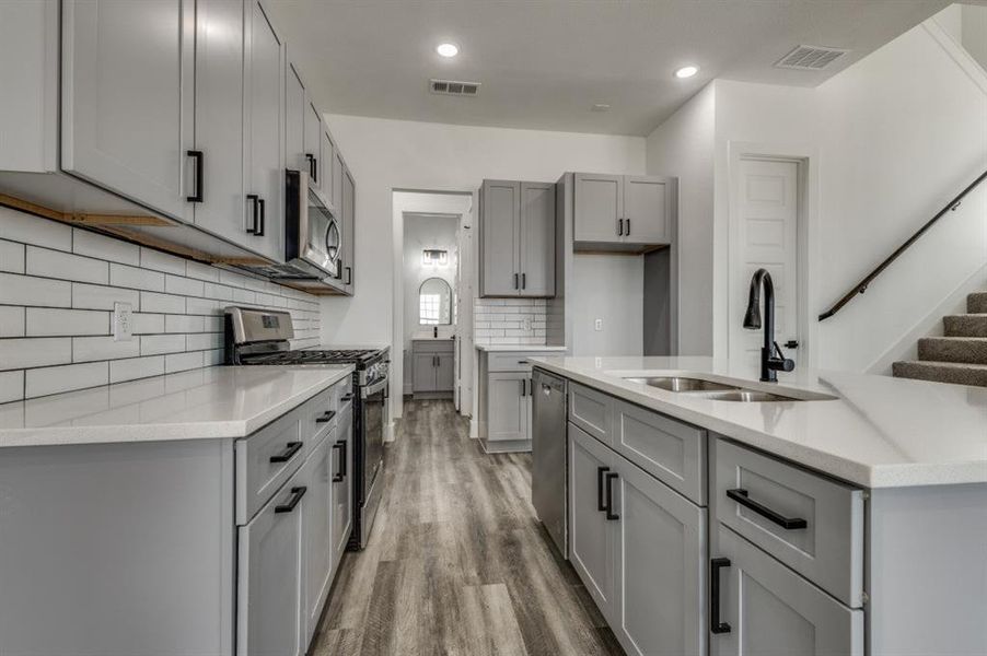 Kitchen featuring sink, tasteful backsplash, light hardwood / wood-style floors, gray cabinets, and appliances with stainless steel finishes