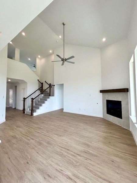 Spacious interior featuring soaring vaulted ceilings, recessed lighting, wood-finish flooring, a contemporary fireplace with a timber mantel, and a staircase with dark wood railings and balusters