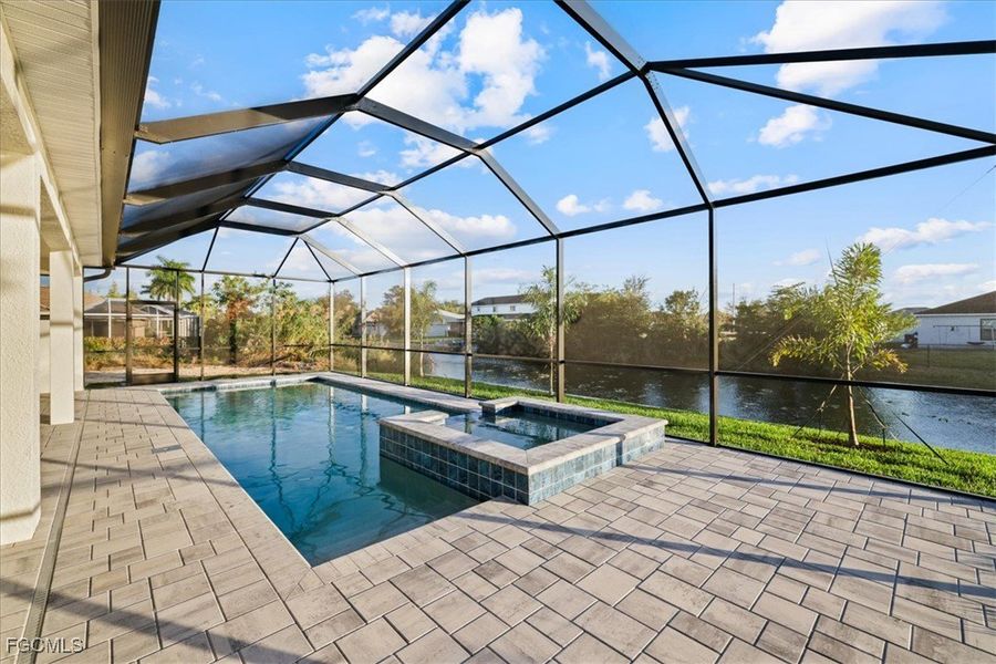 View of pool featuring a sunroom, a water view, a pool with connected hot tub, glass enclosure, and a patio