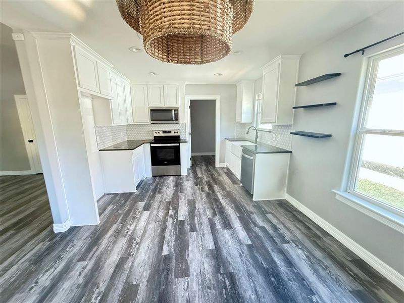 Kitchen with white cabinets, open shelves, appliances with stainless steel finishes, backsplash, and dark wood-style flooring Kitchen with white cabinets, open shelves, appliances with stainless steel finishes, backsplash, and dark wood-style flooring