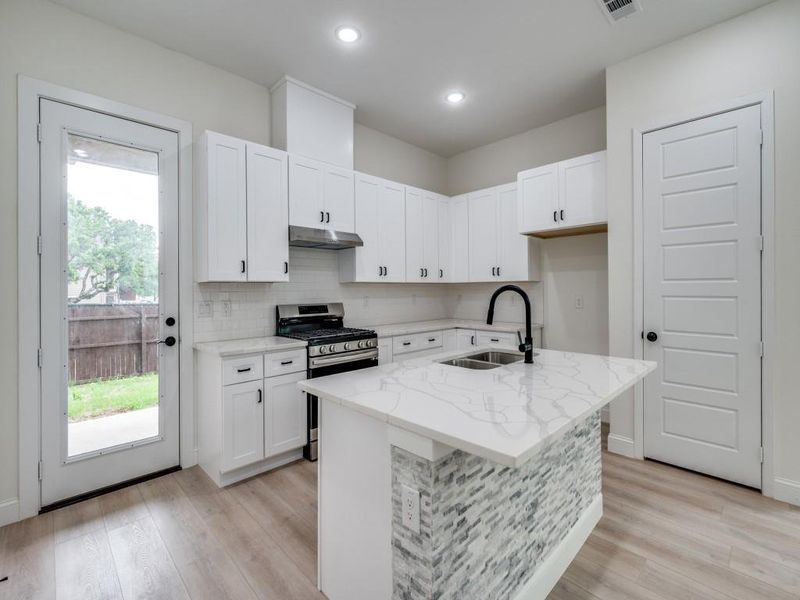 Kitchen with a sink, stainless steel range with gas stovetop, light wood-style flooring, light stone countertops, and white cabinets