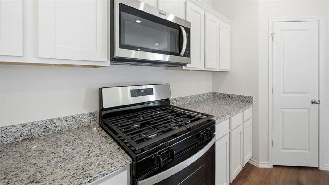 Kitchen featuring appliances with stainless steel finishes, white cabinetry, light stone countertops, and dark wood-style flooring Kitchen featuring appliances with stainless steel finishes, white cabinetry, light stone countertops, and dark wood-style flooring
