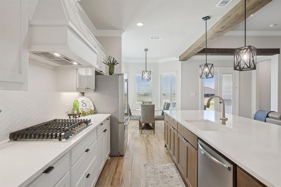 Kitchen with crown molding, light wood-look ceramic tile floors, appliances with stainless steel finishes, light countertops, and white cabinetry