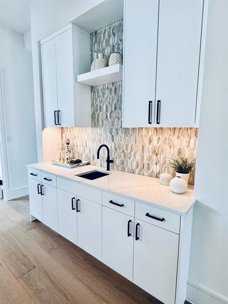 Kitchen featuring white cabinets, decorative backsplash, light stone countertops, and sink