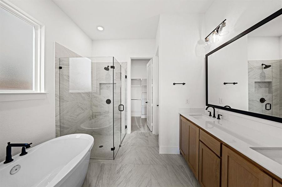 Bathroom with a shower stall, double vanity, a freestanding bath, a spacious closet, and light marble finish flooring