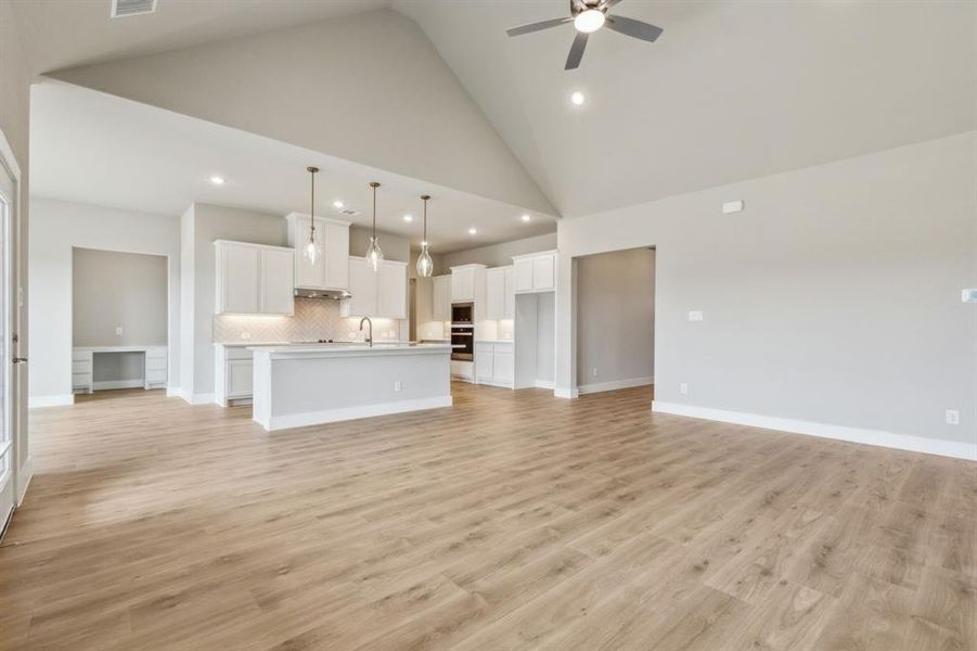 Unfurnished living room with light wood-type flooring, ceiling fan, sink, and high vaulted ceiling