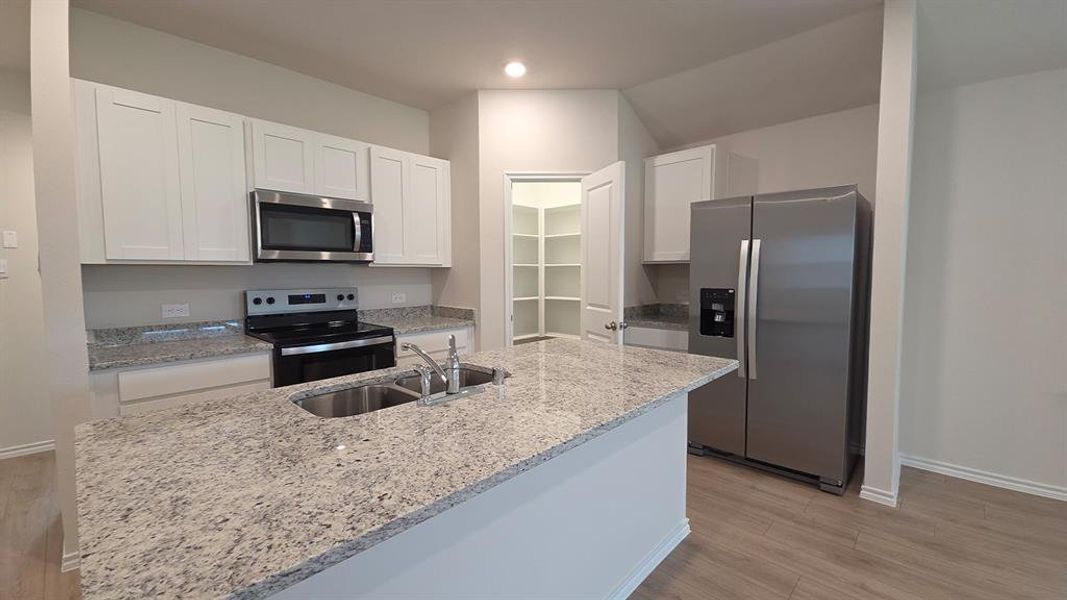 Kitchen featuring an expansive island with an undermount double basin sink, light-toned granite countertops, white shaker cabinetry, stainless steel appliances, and wood-finish flooring