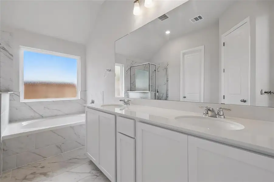 Bathroom featuring marble look tiles, a garden tub, double vanity, a marble finish shower, and vaulted ceiling