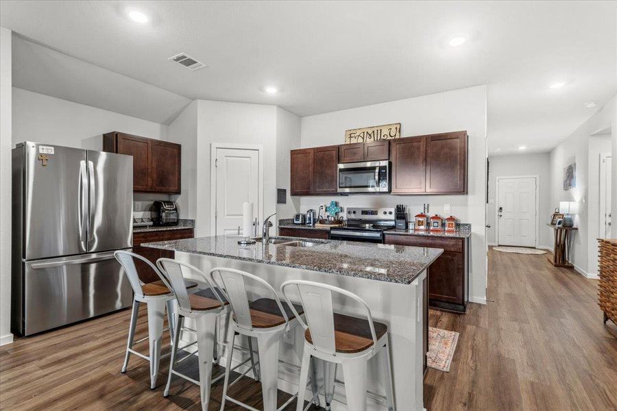 Kitchen with stainless steel appliances, dark stone countertops, an island with sink, a kitchen breakfast bar, and dark wood-style floors