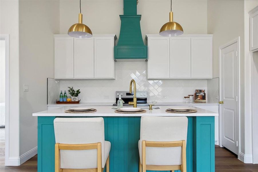 Kitchen with tasteful backsplash, white cabinetry, custom range hood, and decorative light fixtures