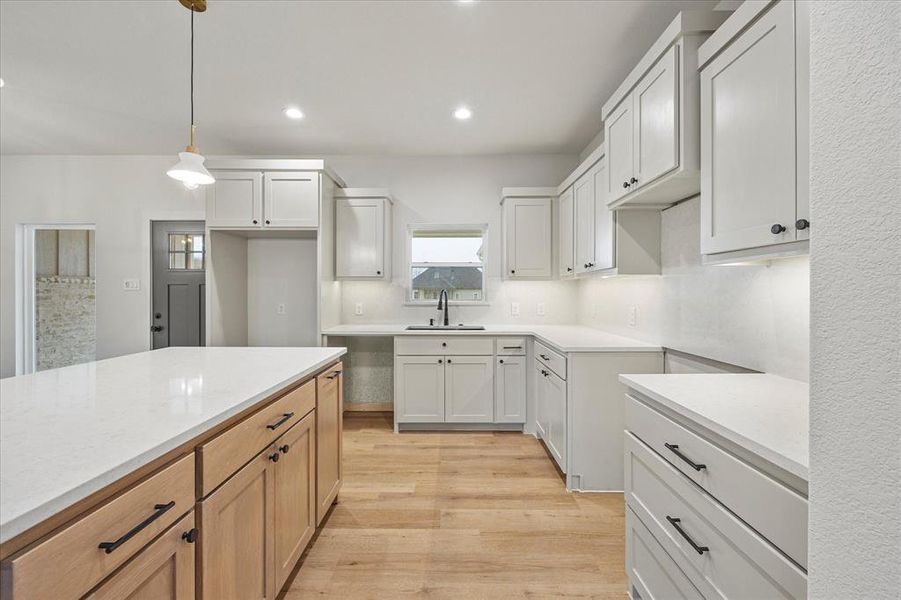 Kitchen with sink, white cabinets, light wood-type flooring, and decorative light fixtures