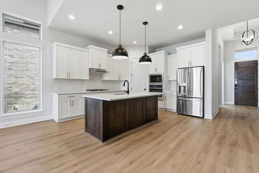 Dual tone kitchen featuring two tone cabinetry, stainless steel appliances, a center island with sink, light wood finished floors, and hanging lights