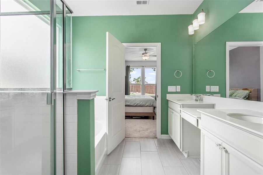 Ensuite bathroom featuring ceiling fan, double vanity, a garden tub, and an enclosed shower