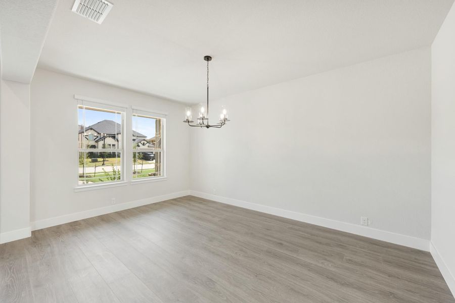 Empty dining room with light wood floors, chandelier, and double windows overlooking neighborhood