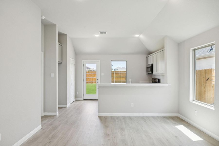 Kitchen featuring light wood finished floors, light countertops, stainless steel microwave, lofted ceiling, and a peninsula