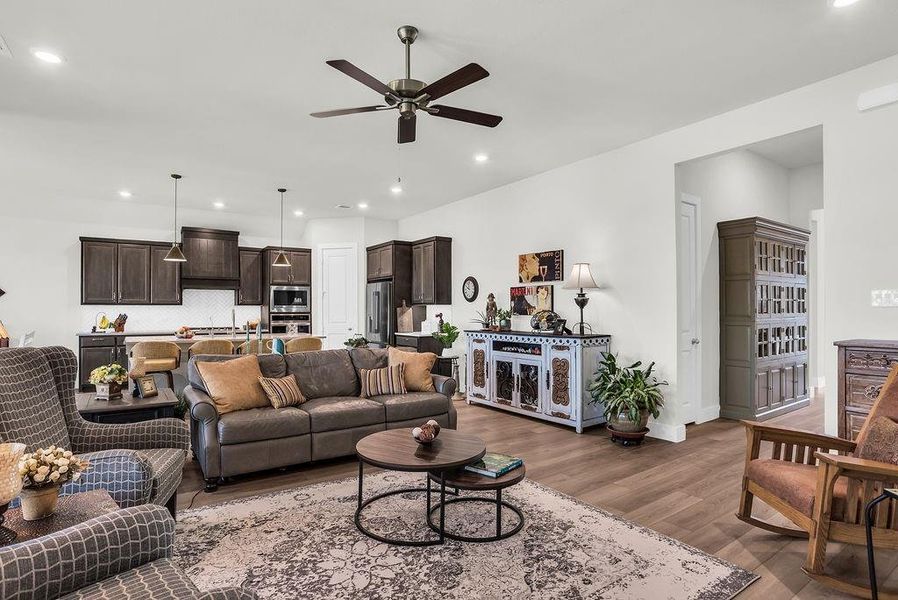 Open-concept living space featuring ceiling fan, ample natural light from multiple windows, an inset electric fireplace, and wood-finish flooring