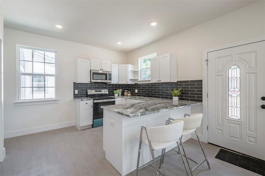 Kitchen with stainless steel appliances, light stone counters, kitchen peninsula, and white cabinetry