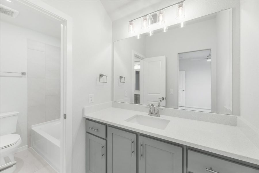 Bathroom with gray vanity cabinets, white quartz countertop, large mirror, and soaking tub with tile surround