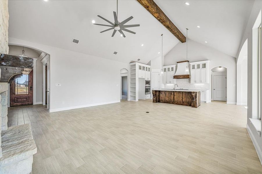 Unfurnished living room with arched walkways, a ceiling fan, high vaulted ceiling, light wood-style flooring, and beamed ceiling