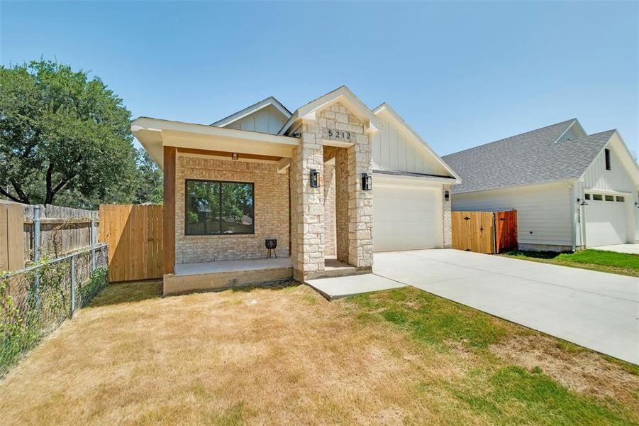 View of front of home featuring board and batten siding, a garage, concrete driveway, covered porch, and stone siding