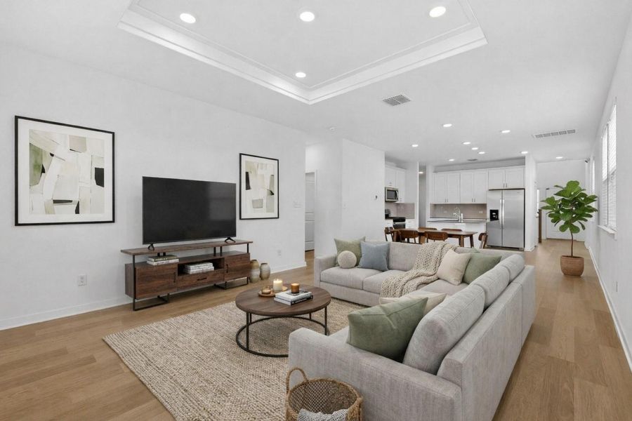 Living area with recessed lighting, a raised ceiling, light wood finished floors, and crown molding