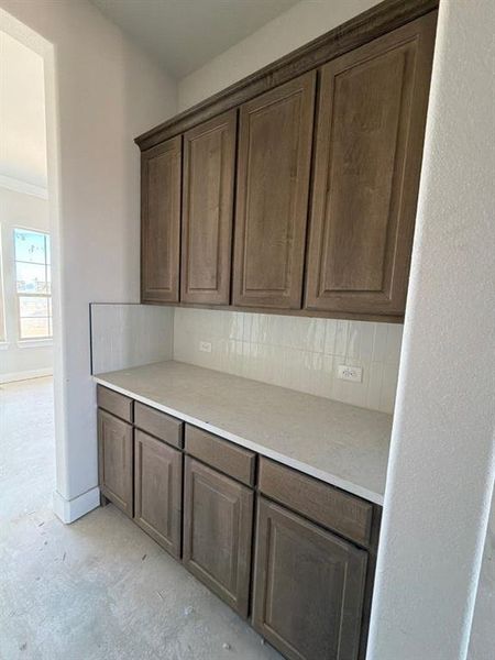 Kitchen with backsplash, ornamental molding, and dark brown cabinetry
