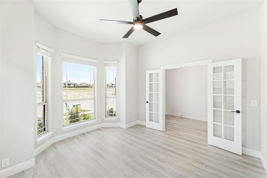 Empty room with light wood floors, bay windows, ceiling fan, and French doors