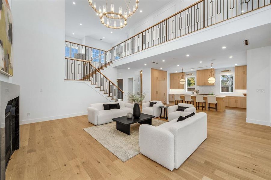 Living area with light wood-style flooring, a fireplace, recessed lighting, a chandelier, and a high ceiling
