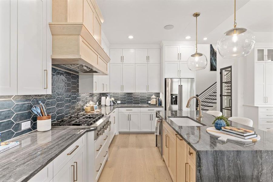 Kitchen featuring dark stone counters, decorative backsplash, appliances with stainless steel finishes, a center island with sink, and light wood-type flooring Kitchen featuring dark stone counters, decorative backsplash, appliances with stainless steel finishes, a center island with sink, and light wood-type flooring