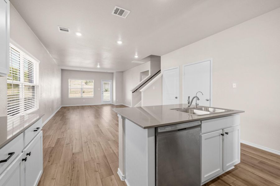 Kitchen with white cabinetry, stainless steel dishwasher, open floor plan, a kitchen island with sink, and light wood finished floors