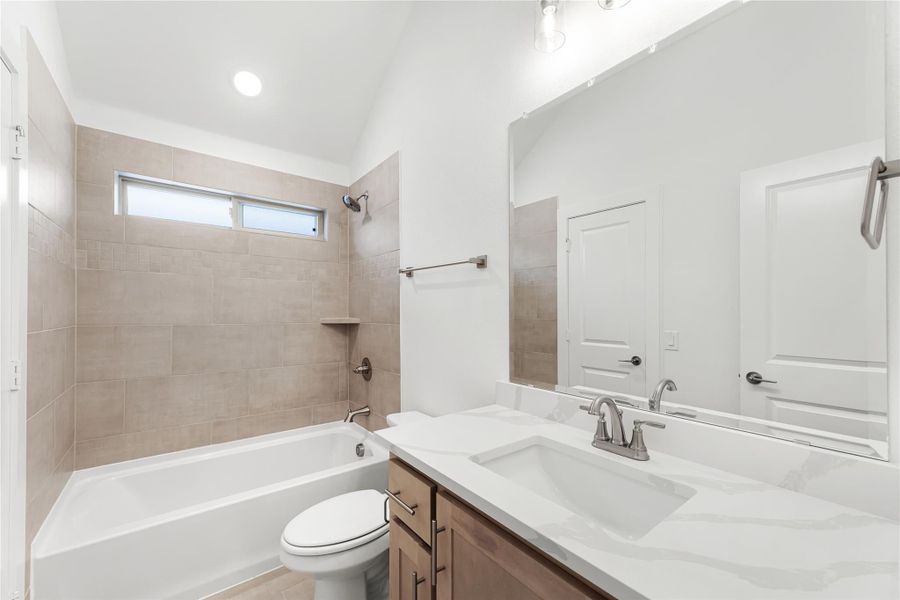 Bathroom with tiled tub surround, white quartz vanity, and vaulted ceiling