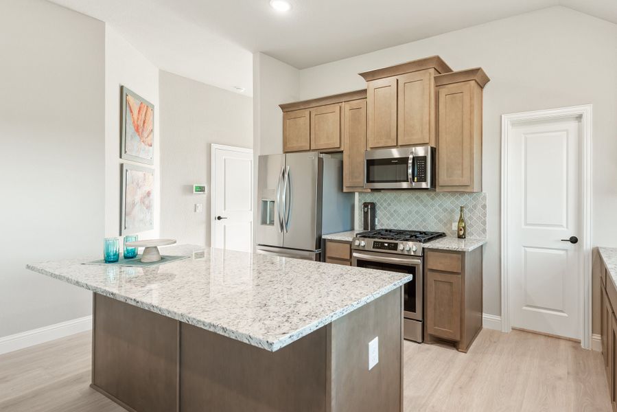Kitchen with granite island, tan cabinets, stainless steel appliances, and tiled backsplash Kitchen with granite island, tan cabinets, stainless steel appliances, and tiled backsplash
