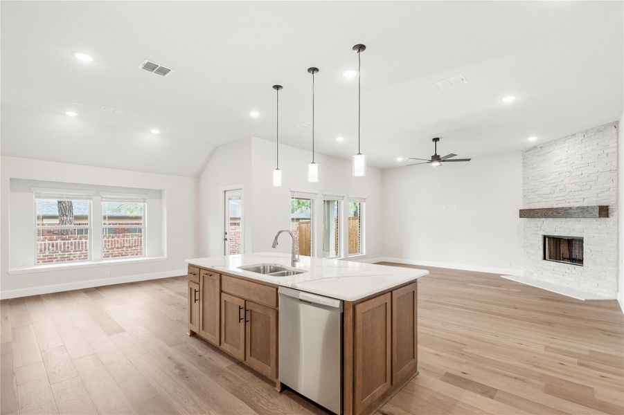 Kitchen island with wood cabinets and quartz countertop open to living room with stone fireplace and hardwood floors
