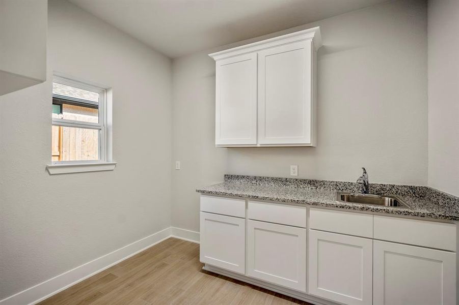 The utility room, featuring sleek granite countertops and crisp white cabinetry, it offers ample storage and workspace for all your day-to-day needs. The elegant sink provides convenience, ensuring your chores become a breeze in this thoughtfully designed space.