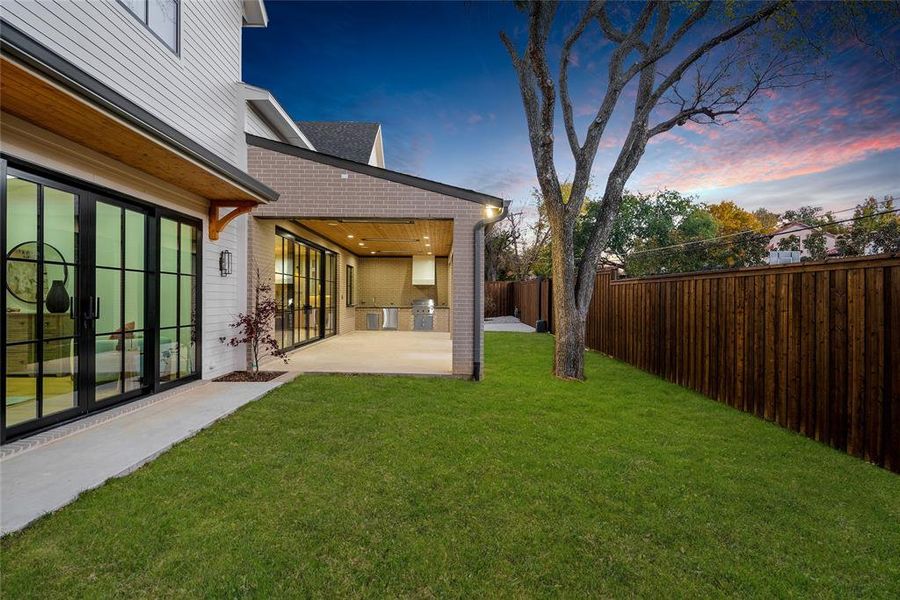Expansive backyard featuring a manicured lawn, full privacy fencing, and mature trees
