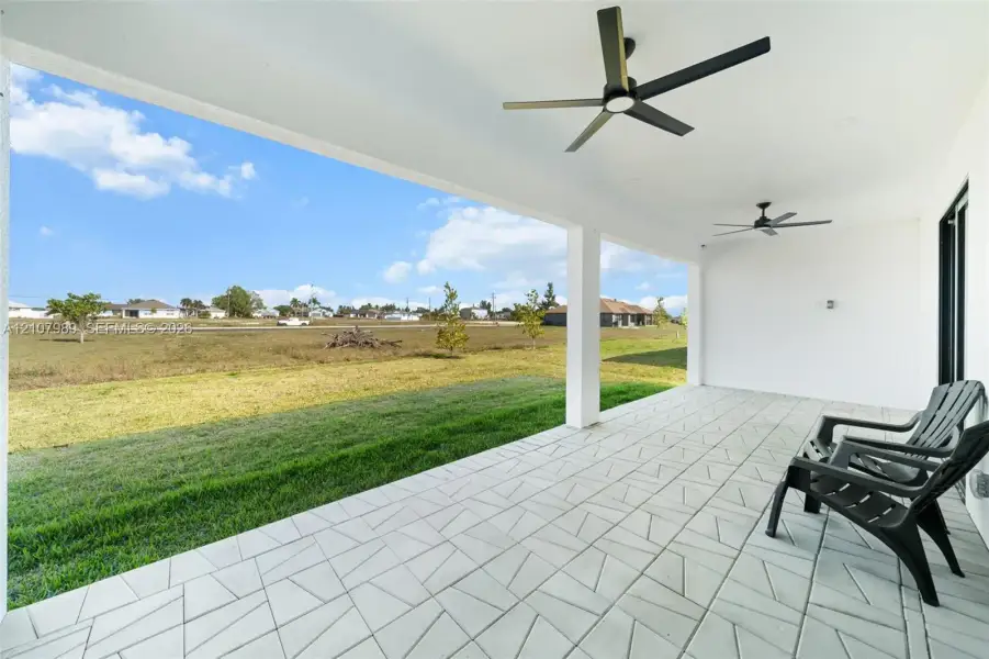 Covered patio featuring patterned concrete tile flooring, dual ceiling fans, and structural support columns overlooking an open grass lawn Covered patio featuring patterned concrete tile flooring, dual ceiling fans, and structural support columns overlooking an open grass lawn