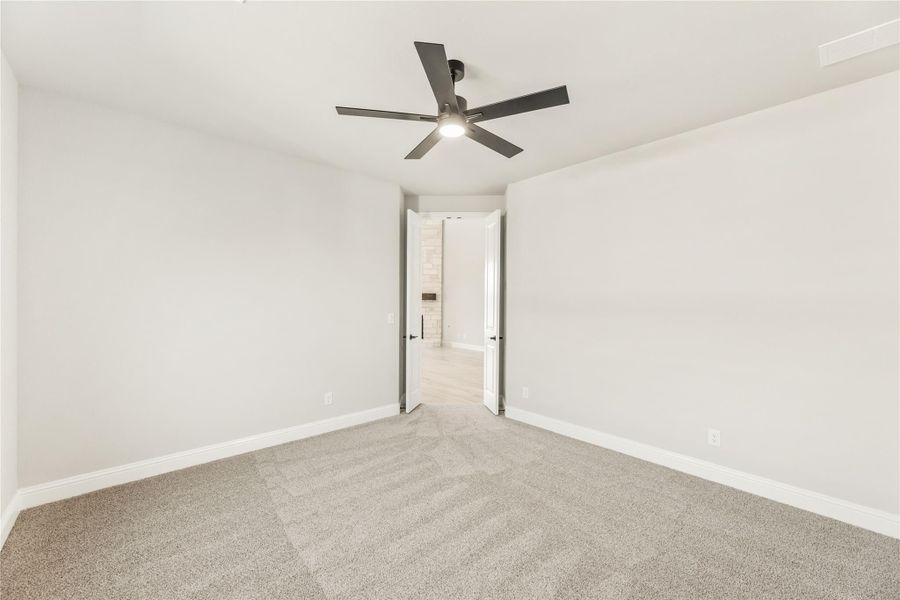 Empty bedroom with gray carpet, white walls, ceiling fan, and open door to bathroom Empty bedroom with gray carpet, white walls, ceiling fan, and open door to bathroom